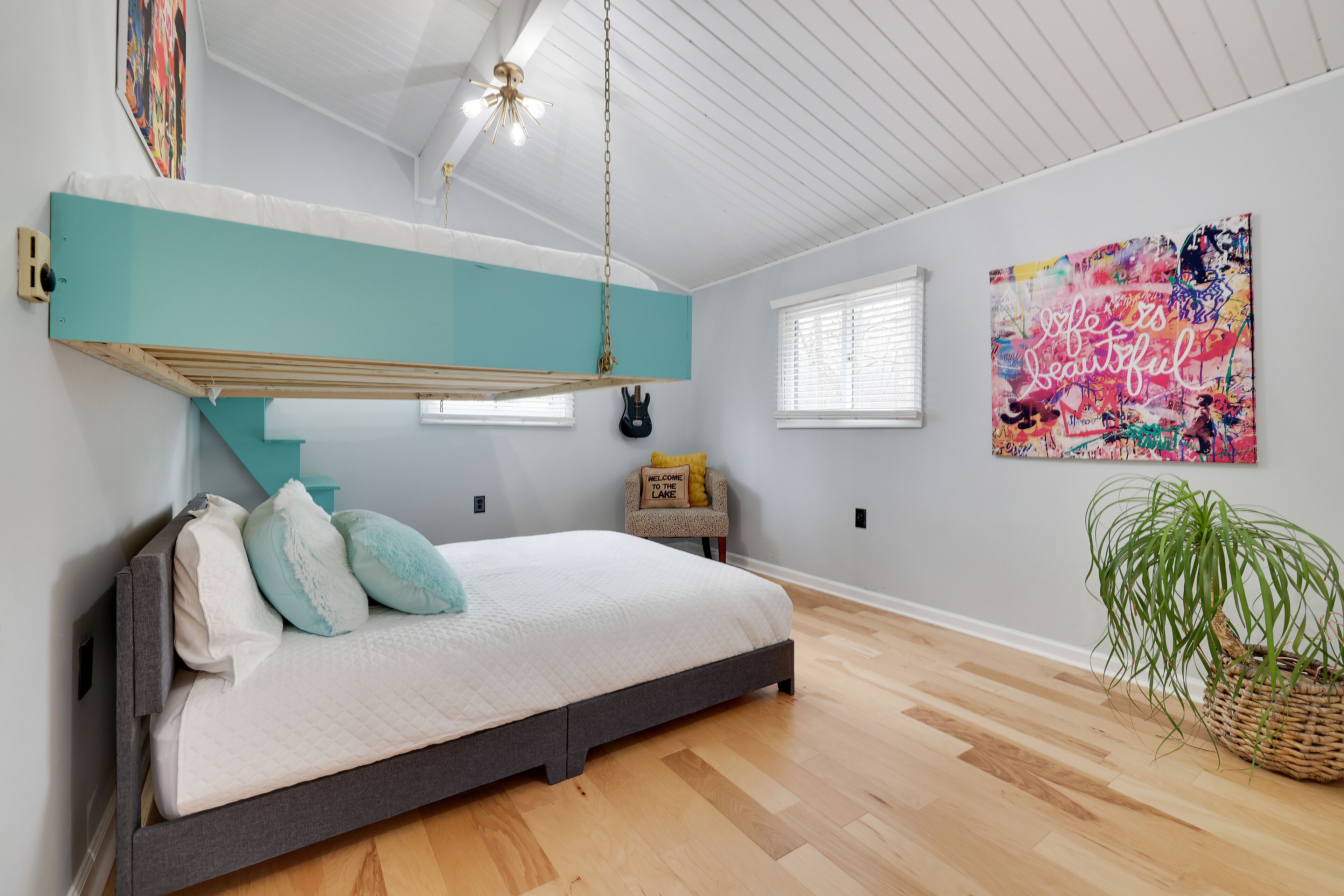 A bedroom with a bed, a hanging chair, a plant, and artwork on the wall.