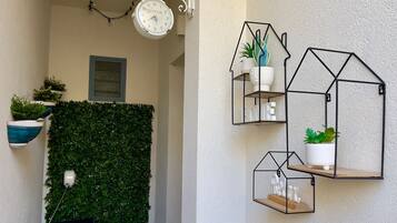 Una pared con un reloj, estanterías geométricas y plantas en macetas.