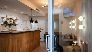 A modern reception area with a wooden reception desk, a glass partition, and a dining area with a table and chairs. - Incanto B&B (Cefalù)