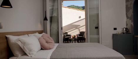 A bedroom with a bed, a nightstand, a desk, a chair, and a balcony with a view.