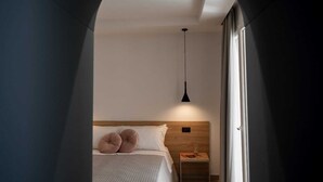 A bedroom with a bed, a bedside table, a hanging light, and an arched doorway. - Incanto B&B (Cefalù)