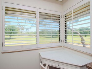 A room with a white desk and two windows with white blinds.