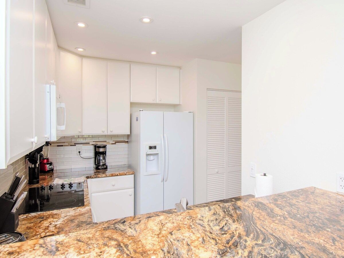 A modern kitchen with white cabinets, a built-in oven, a refrigerator, and a granite countertop.