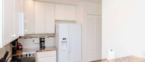 A modern kitchen with white cabinets, a built-in oven, a refrigerator, and a granite countertop.