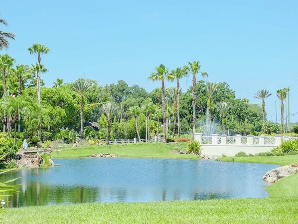 A tranquil outdoor setting with a pond, lush greenery, and a white fence.