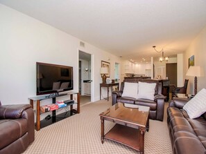 A living room with a flat-screen TV, leather sofas, a coffee table, and a patterned carpet.