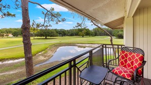 Un balcón con vistas a un campo de golf, una silla estampada de color rojo y una pequeña mesa.
