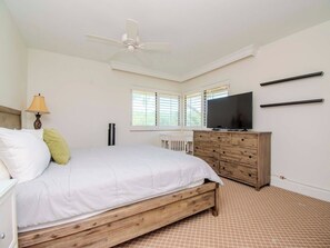 A bedroom with a bed, a TV, a dresser, and a ceiling fan.