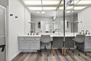 Une salle de bain moderne avec un grand miroir, un meuble-lavabo blanc et deux chaises grises.