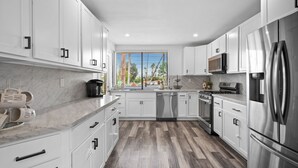 A modern kitchen with white cabinets, stainless steel appliances, and a large window with a view of trees. - Newly Remodeled Home @ the Omni at Rancho Las Palmas in Rancho Mirage! (Rancho Mirage)