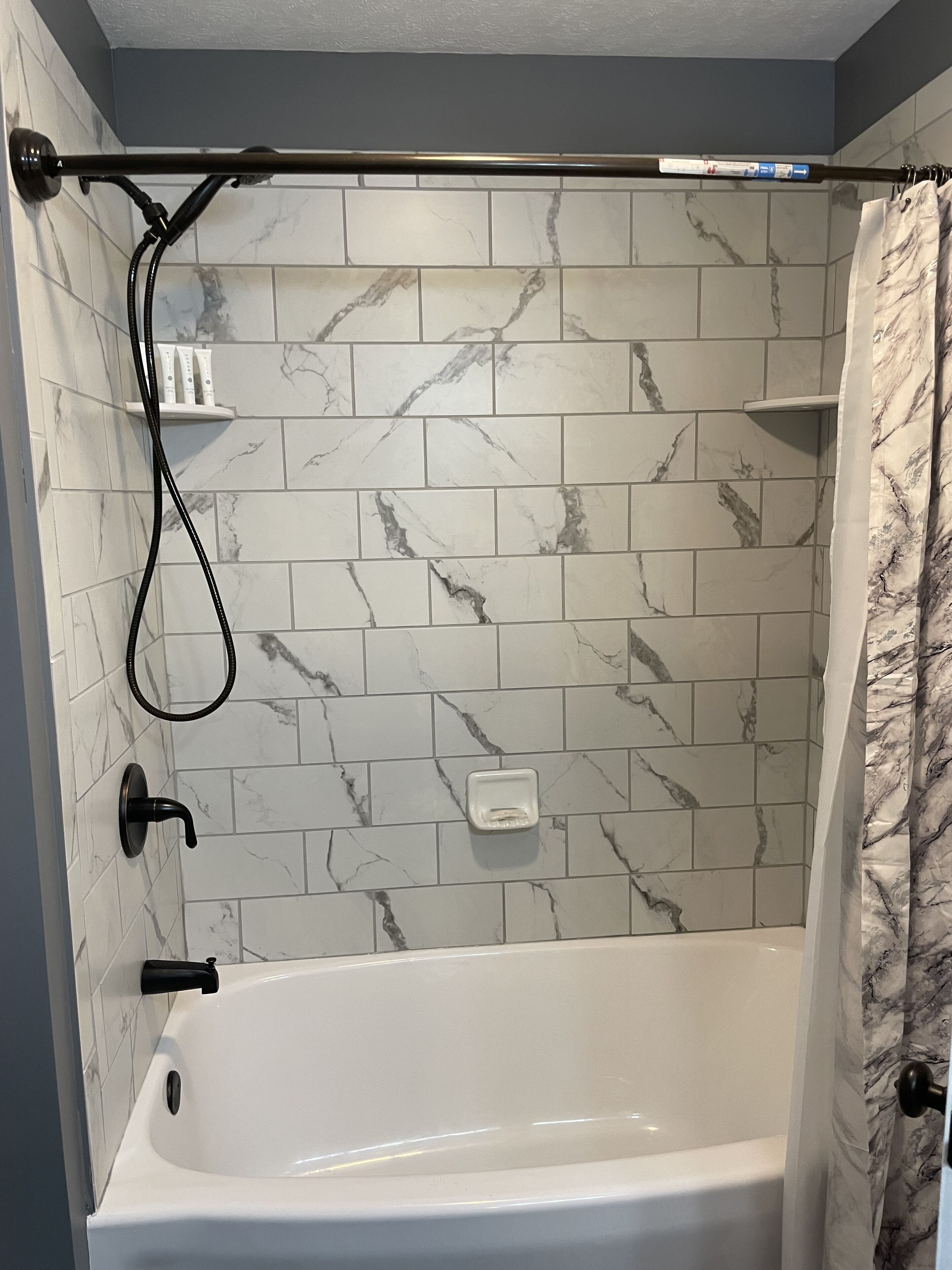Ein Badezimmer mit einer weißen Badewanne, einer Duschvorhang und einer Wand mit Marmor-Musterfliesen.