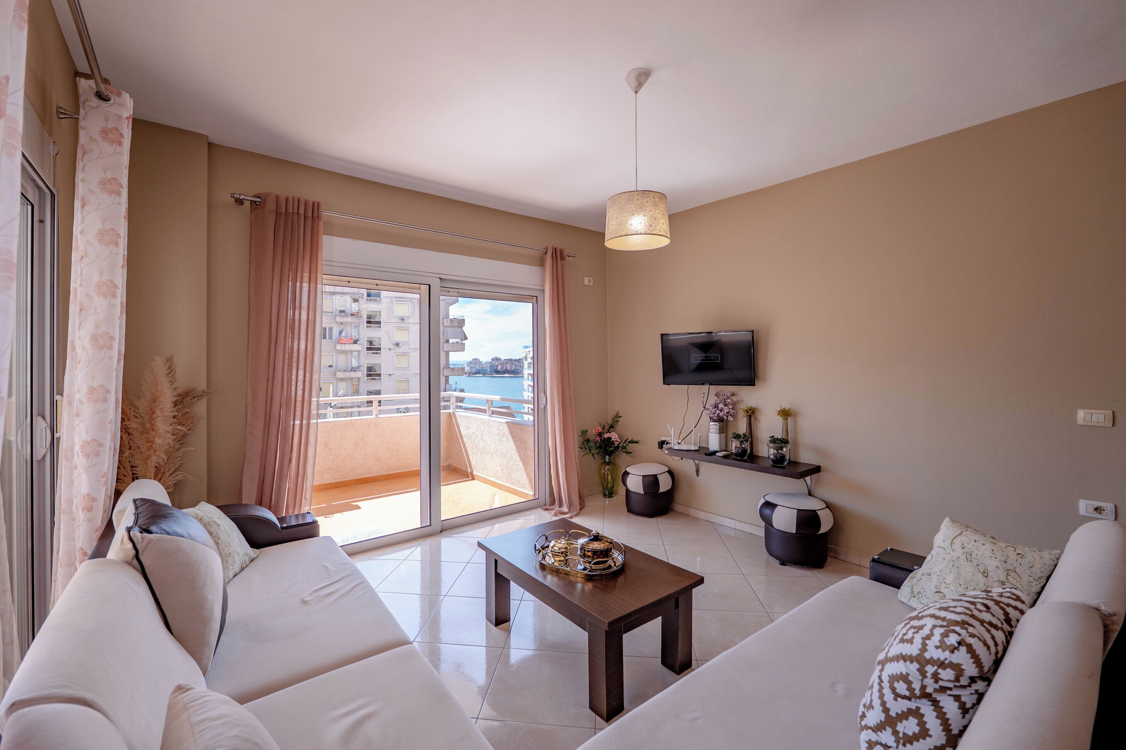 A modern living room with a sofa, a coffee table, a TV, and a balcony with a view.