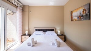 A hotel room with a bed, two bedside tables with lamps, a painting on the wall, and an air conditioning unit.
