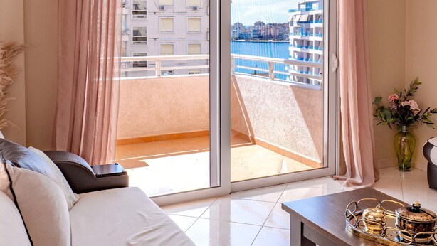 A modern living room with a sofa, a coffee table, and a view of a balcony with a cityscape.