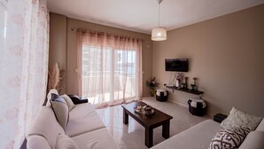 A living room with a sofa, a coffee table, a TV, and a window with sheer curtains.