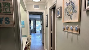A hallway with wooden flooring, a dining area with chairs, and a wall-mounted art piece.