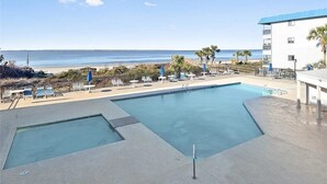 A pool area with a view of the beach, lounge chairs, and umbrellas.