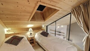 A cozy cabin room with two beds, a small table, a lamp, and a window with curtains.