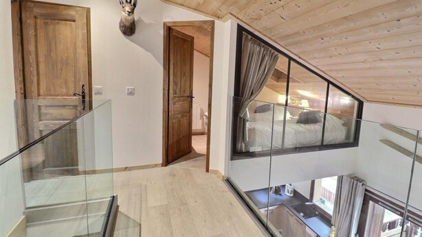 A modern interior with a glass staircase, wooden ceiling, and a view of a bedroom with a bed and curtains.