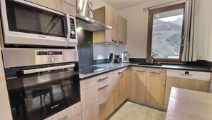 A modern kitchen with stainless steel appliances, wooden cabinets, and a window with a view of the countryside.