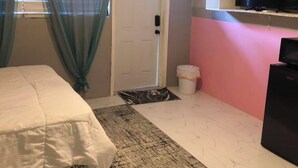Ein Schlafzimmer mit einem Bett, einem Fernseher, einer Tür und einer kleinen Mülltonne.