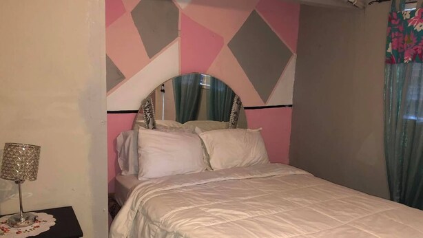 Ein Schlafzimmer mit einem Bett, einem Nachttisch mit Lampe und einer Wand mit geometrischen Mustern.
