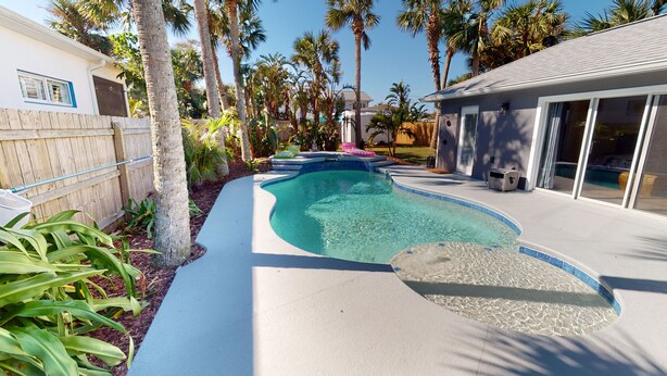 A swimming pool with a tiled edge, surrounded by palm trees and a wooden fence.