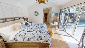 A bedroom with a large bed, a wicker chair, and a view of the outdoors through a sliding door.