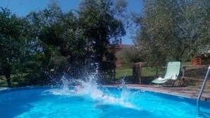 Une piscine à l’eau d’un bleu cristallin, entourée d’arbres et bordée d’une terrasse en bois.
