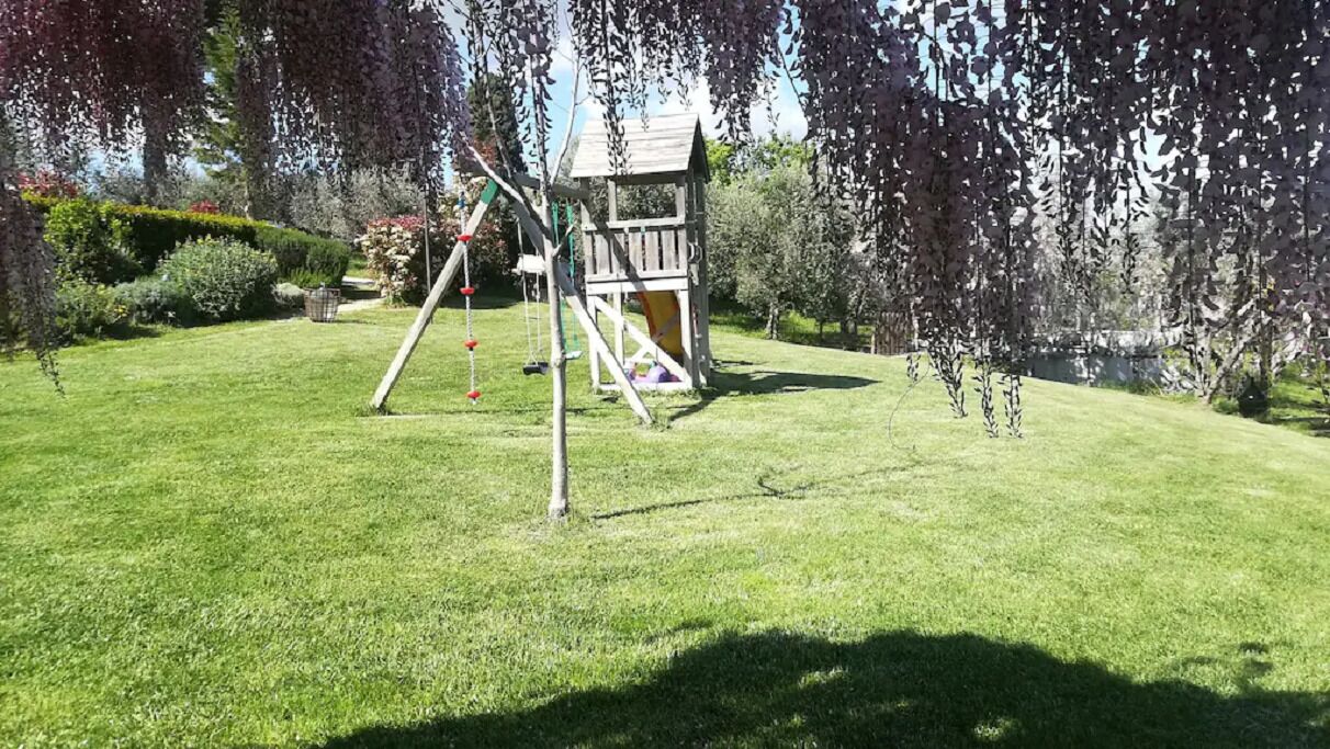 A playground with swings and a slide, surrounded by well-maintained grass and trees.