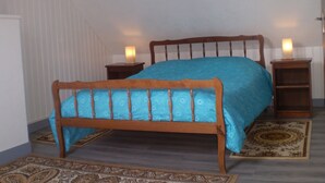 Une chambre avec un lit en bois, deux tables de chevet ornées de bougies, un tapis à motifs et un tableau encadré au mur.