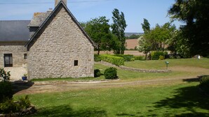 Un bâtiment en pierre doté d’un toit triangulaire, entouré d’une pelouse bien entretenue et d’arbres.