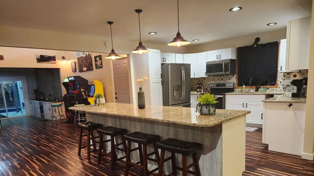 Una cocina moderna con una isla central, taburetes de bar, iluminación colgante y vistas al área de estar.