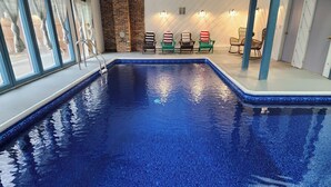 Una piscina interior con suelo de baldosas azules, pared de ladrillo y varias sillas con fundas a rayas y de colores sólidos.