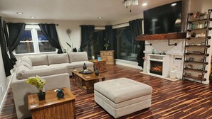 Una sala de estar con sofá, reposapiés, mesa de centro, chimenea y televisor montado en la pared.