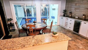 Una cocina con encimera de granito, sillas de madera, una mesa de comedor y vistas a una piscina a través de puertas de vidrio.