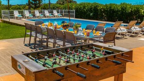 Ein Poolbereich mit Tischfußball, Liegestühlen und einem Esstisch, der für eine Mahlzeit gedeckt ist.