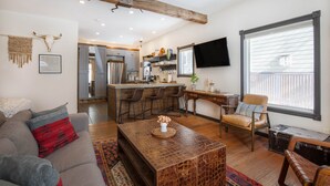 A spacious living area with a sofa, coffee table, and a dining area with chairs and a kitchen in the background. - Pac. Street Studio: Style & space in heart of town (Telluride)