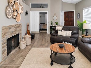 A living room with a fireplace, a leather sofa, a round coffee table, and a variety of decorative items. - Pet-Friendly 3BR | Fenced Yard | Community Pool (Chandler)