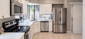 A modern kitchen with stainless steel appliances, white cabinetry, and a window providing natural light.