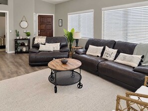 A living room with a brown leather sofa, a round coffee table, and a small side table. - Pet-Friendly 3BR | Fenced Yard | Community Pool (Chandler)