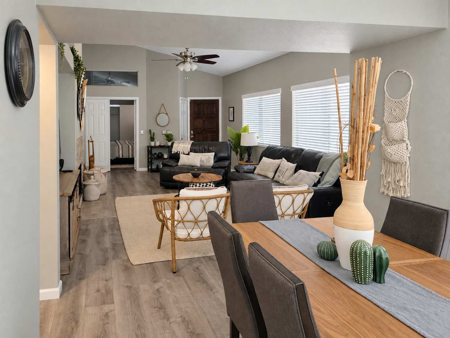 A modern living room with a dining area, a black leather sofa, a wooden dining table, and a ceiling fan.