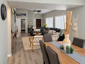Un salon moderne comprenant un coin repas, un canapé en cuir noir, une table à manger en bois et un ventilateur de plafond.