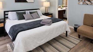 A bedroom with a bed, bedside tables, a chair, a bathroom with a mirror, and artwork on the walls.