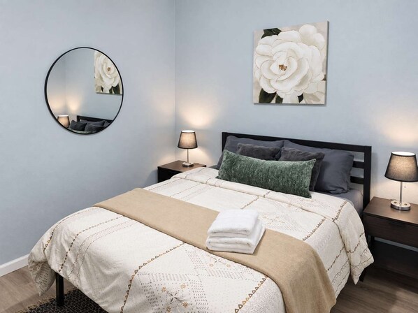 Une chambre à coucher avec un lit, deux tables de chevet, un miroir rond et un grand tableau représentant des motifs floraux accroché au mur.