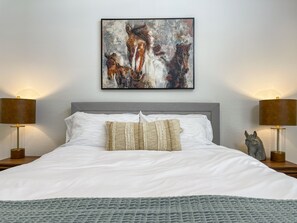 Ein ordentlich bezogenes Bett mit weißen Leinen und zwei Zierkissen, begleitet von je einer Nachttischlampe mit klaren Gläsern.