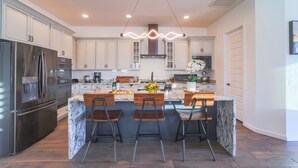 Une cuisine moderne dotée d’un îlot central, d’appareils électroménagers en acier inoxydable et d’un luminaire suspendu.