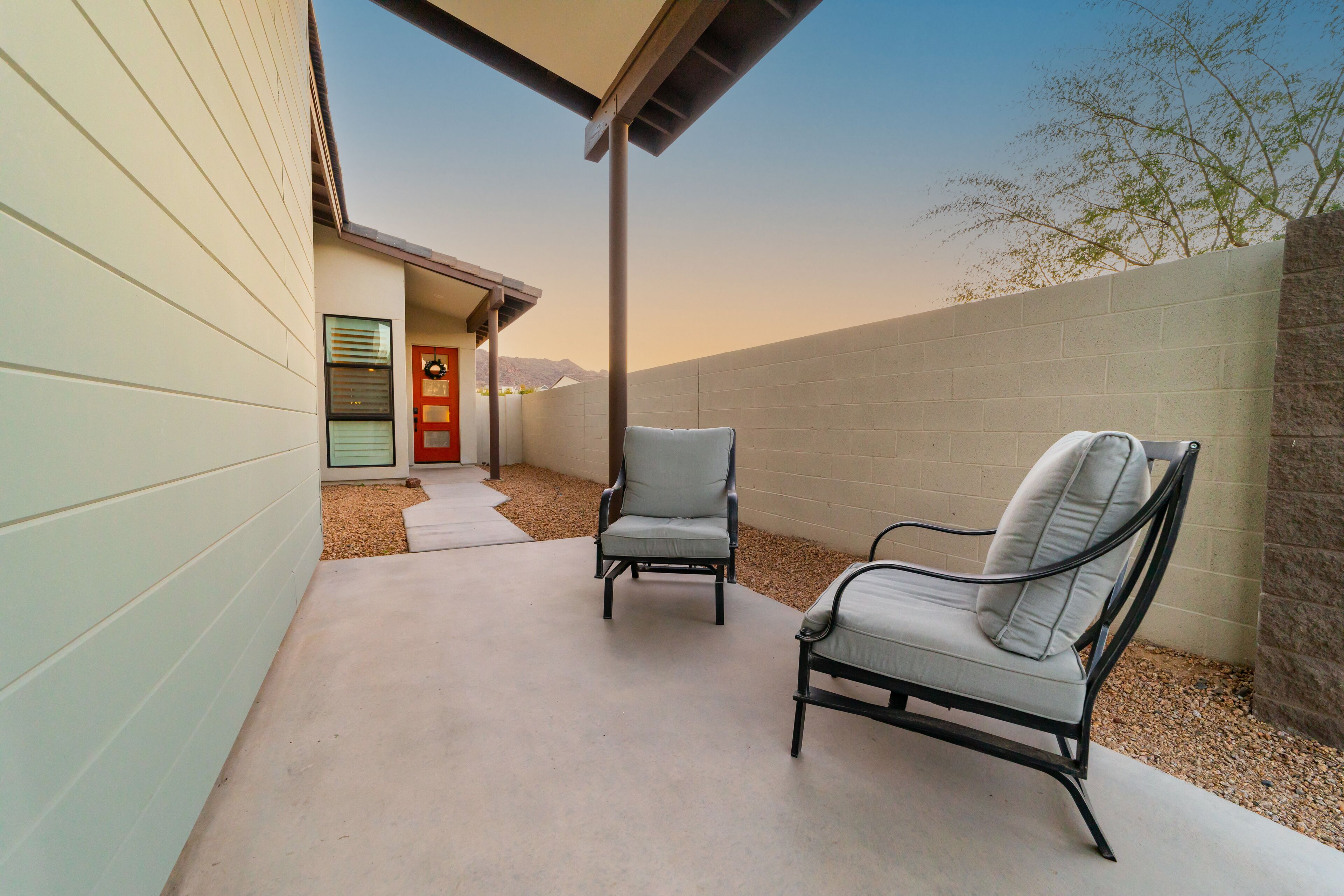 A patio area with two chairs and a concrete floor, adjacent to a building with a door and a window.