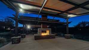 Une terrasse extérieure dotée d’un foyer, de bancs et d’une structure en forme de pergola.