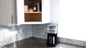Een keuken met een koffiezetapparaat op het aanrecht, een kastje met een fles Kirkland koffie, en een doos Bigelow Vanilla koffie.